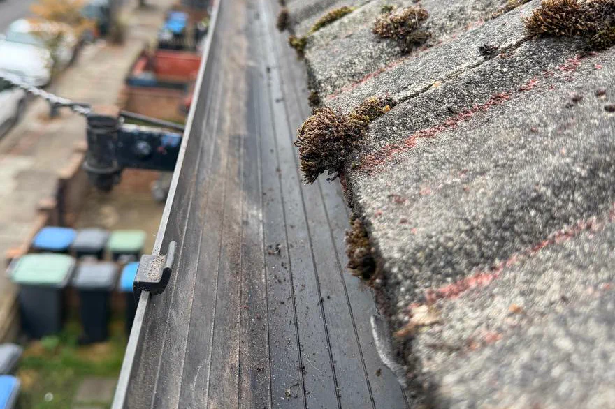 The same gutter run after clearing: the channel empty and running clear, with the moss still on the tiles above