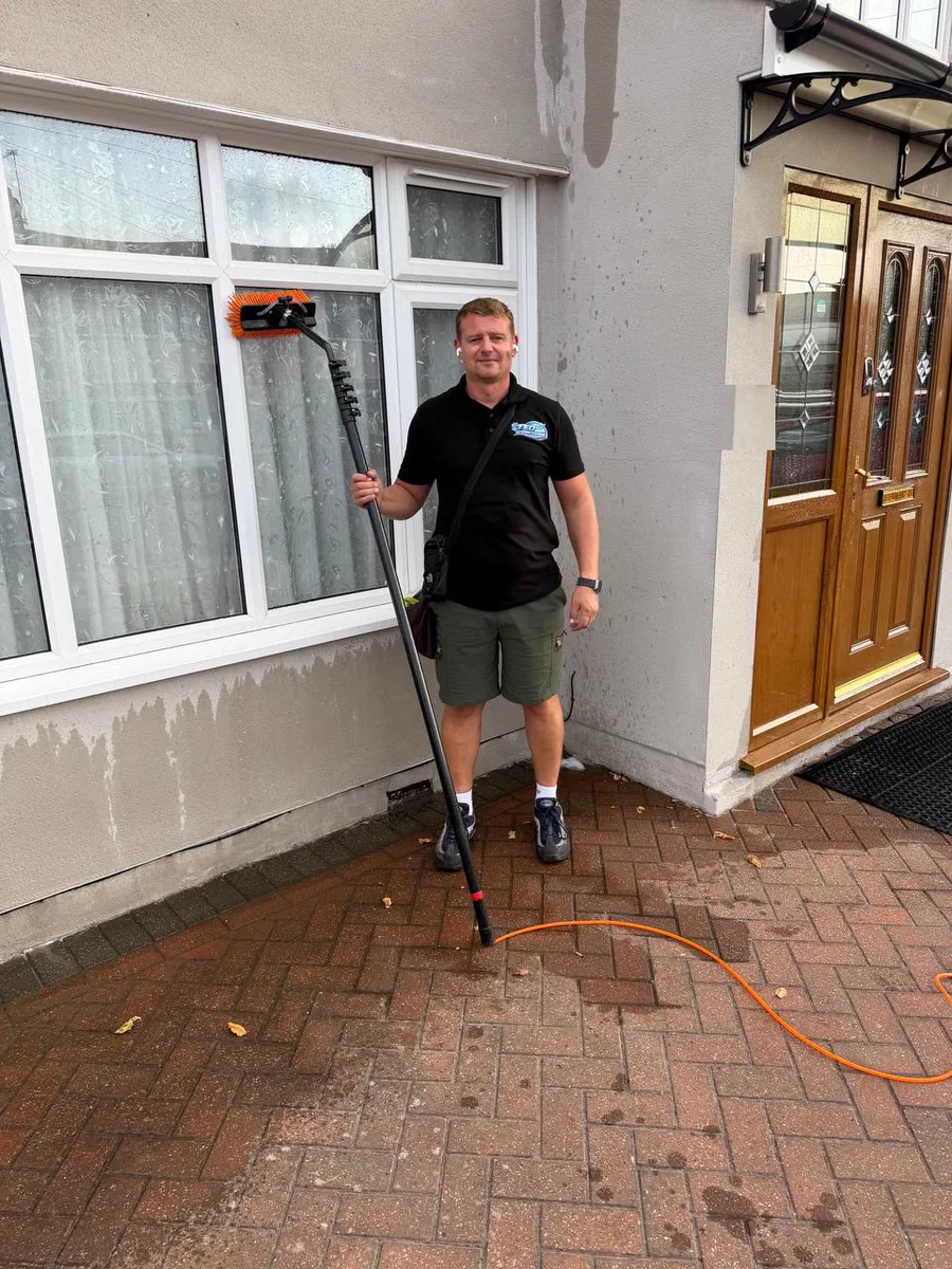 Teo in a Teo Exterior Cleaning polo holding a water-fed pole at the corner of a house with a wooden front door