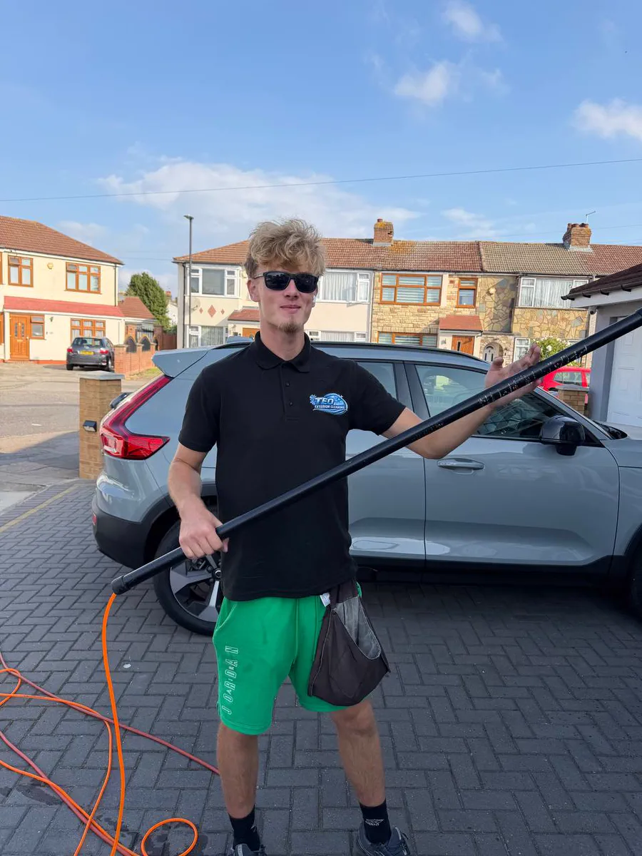 His son, who cleans alongside him, holding a water-fed pole on a North London street